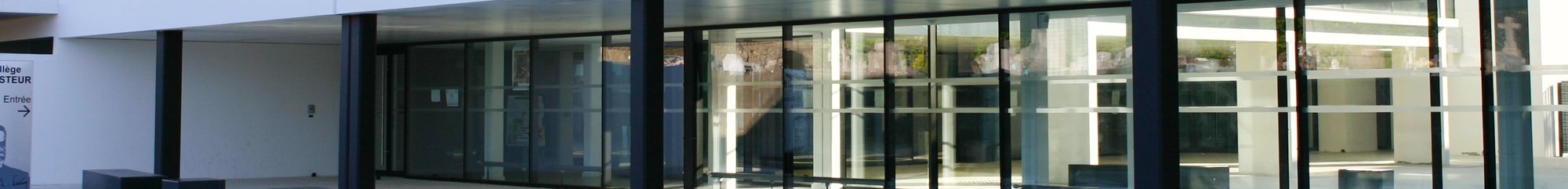Façade moderne en grandes baies vitrées encadrées de poteaux sombres, avec un panneau indiquant l'entrée sur la gauche.