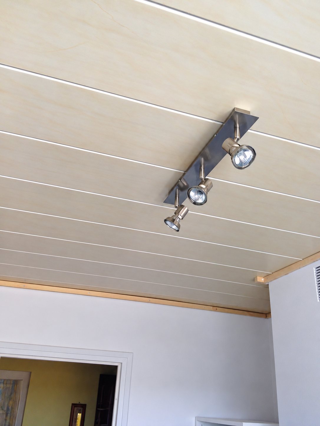 Plafond en lambris clair avec une rampe de trois spots